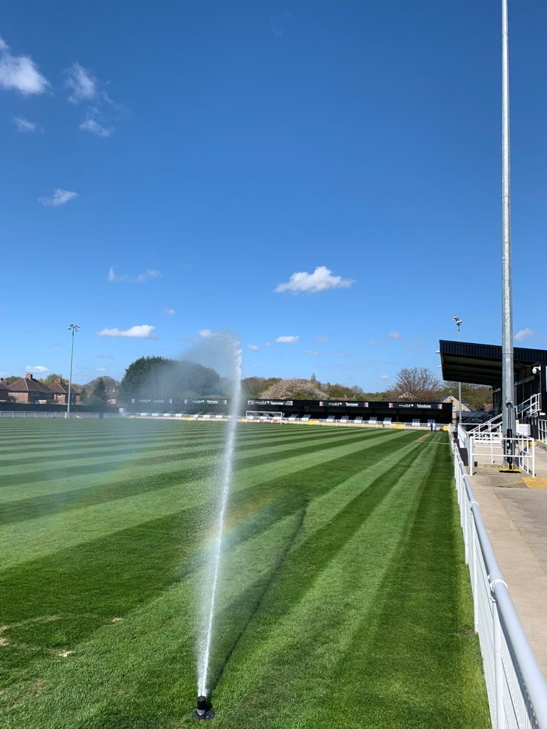 A sprinkler covers a football pitch in water