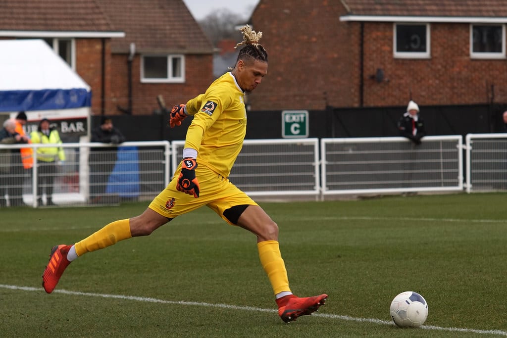 Goalkeeper in yellow kit strikes a goal kick