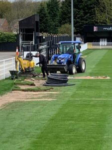 Tractor and people install drains in football pitch