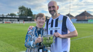 Judith Gates, Founder of Head For Change, with Mark Solan, Founder of Solan Connor Fawcett Family Cancer Trust, holding the Bill Gates Memorial Cup after 2021’s game at The Brewery Field.